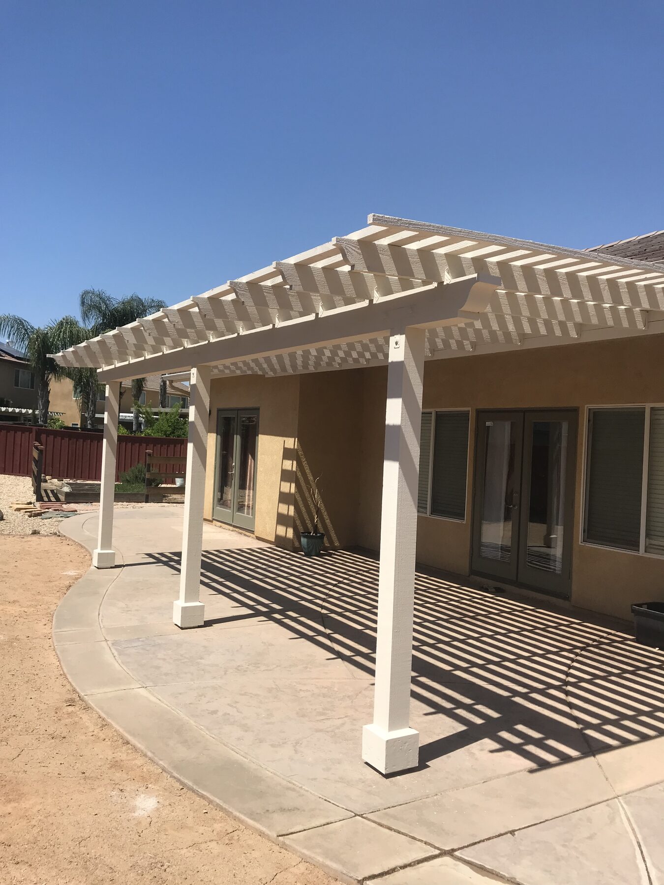 New white wood lattice patio cover on a tan stucco house with a fresh concrete slab under a blue sky