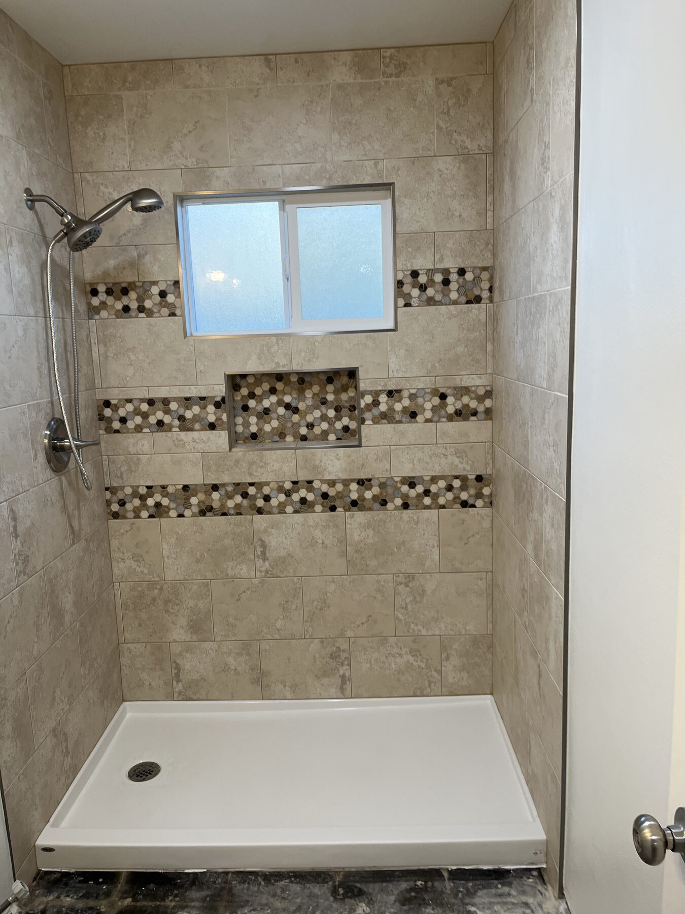 Shower in travertine-look tile with a glass mosaic band and a window